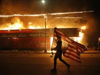 متظاهر يحمل علم الولايات المتحدة مقلوبًا، بجوار مبنى محترق في مينيابوليس